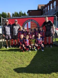 Quarrydale U8's team with their 3 coaches, holding their trophy in front of a large Quarrydale banner.